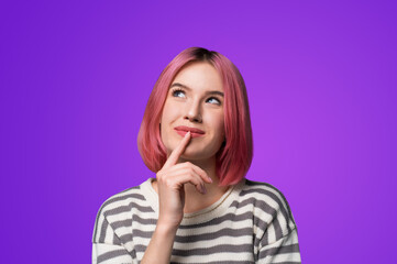 Portrait ad image - mysteriously grinning smile look up thinking gladly pink hair woman wear grey striped sweater jumper, hold finger over her she lips, isolated violet purple background.