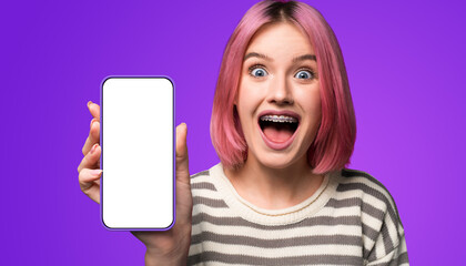 Shock astonished very happy pink woman wear braces, opened mouth, show cell phone, modern smartphone mobile phone cellphone with blank white mock screen, isolated purple background. Online offer ad.