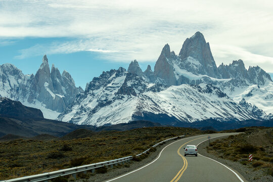 Carro viajando por estrada sinuosa e ao fundo montanhas nevadas do Fitz Roy nas cordilheiras dos andes.