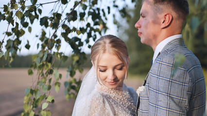 Bride and groom touching and enjoying each other against a backdrop of birch tree branches.