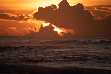 The sun sinks below the horizon, casting a warm glow over the ocean with scattered clouds in the...