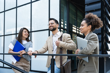 Three young business people talking to each other while standing outdoors of office building with...