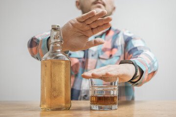 Man refusing alcohol, glass with alcohol drink and bottle of whiskey or brandy on a table,...