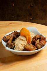 A plate of fried pork with Alentejo-style migas, a dish made from breadcrumbs, garlic, and herbs, topped with an orange slice. Captured in a rustic restaurant setting, it exudes warmth and tradition.