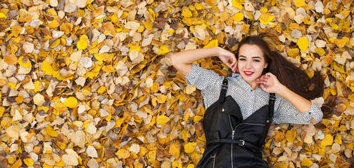 Close up portrait beautiful girl in a black leather dress lies on fallen autumn leaves