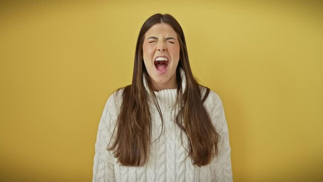 Furious young hispanic woman, beautiful in her anger, screams in frustration over isolated yellow background. enraged in her sweater, she stands fiercely before the cutout wall, her rage boiling over.