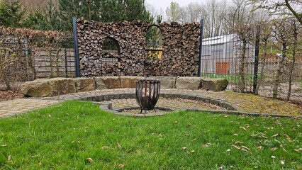 A large fire pit with wood in it sits in front of a stone wall