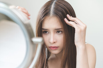 Damaged hair symptom, problem hair fall asian young woman, girl worry about balding, looking at scalp in mirror, hand in break into front hair loss, thin problem. Health care treatment for beauty.