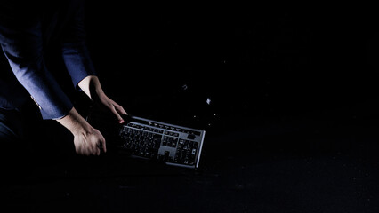 Man banging and hitting computer keyboard on a hard floor, isolated on a black background, slow motion shot. Job anxiety, employee burnout, and modern lifestyle concepts.