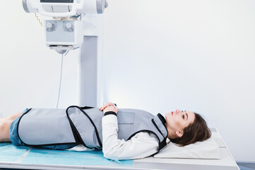 Female patient in a protective suit lying on bed  in modern X-ray machine for scanning her leg or knee for injuries and fractures. 