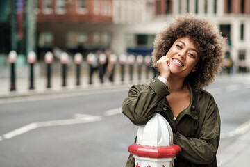 Happy mixed race woman leaning on bollard in a London street.