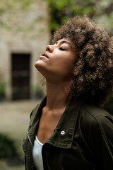 Relaxed young woman breathing fresh air with eyes closed outdoors.