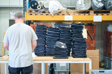 A pile of raw denim jeans fresh off a production line in a denim factory. Industrial fabric and...
