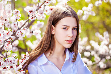 Pretty teen girl are posing in garden near blossom cherry tree with white flowers - obrazy, fototapety, plakaty