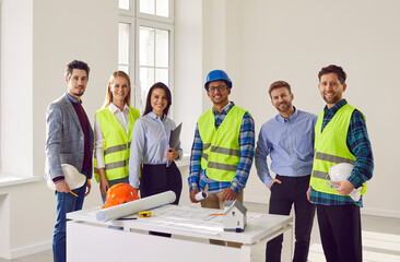 Team of construction workers and engineers in hardhats discussing project. Group of cheerful professional builders in hardhats looking at camera at construction site