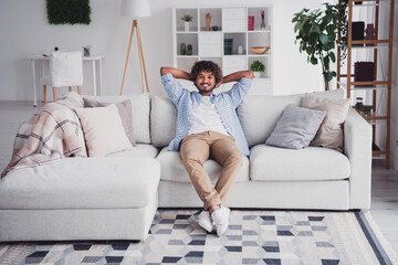 Photo of cheerful positive guy dressed plaid shirt arms behind head enjoying weekend sitting sofa indoors room home house