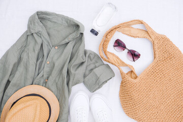  Look of women for spring summer. Linen shirt, white sneakes, Straw bag for beach, bottle of water, straw hat and sunglasses on white background. Summer and beach accessories.