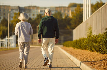 Back view of senior retired couple wearing sportswear walking along a path in park having sport workout. Elderly men and women exercising outdoors. Workout in nature and healthy lifestyle concept.