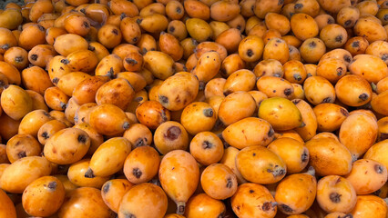 Pile of freshly picked ripe juicy bright orange medlar loquat fruits at farmers market.