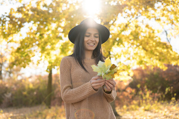 Beautiful hispanic woman with autumn yellow leaves. Portrait of joyful woman in park during fall....