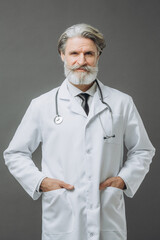 Gray-haired male doctor in a white medical coat with a phallendoscope on a gray background.