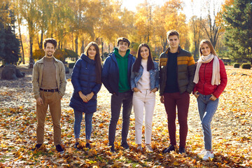 Portrait of a group of happy friends walking in the autumn park. Young caucasian people girls and boys looking at the camera and smiling outdoors. Friendship and togetherness concept.