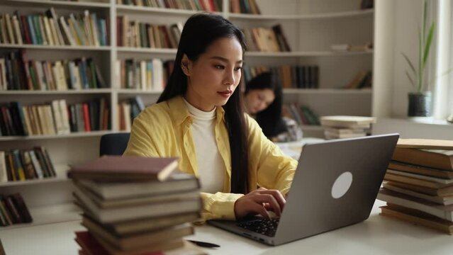 Charming confident asian girl preparing for exam at university studying and typing at library workplace Pretty student looking at laptop computer screen indoors Distance remote education