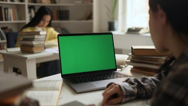 Over-the-shoulder view of student looking at laptop green screen chroma key template mock up for design advertising at university library