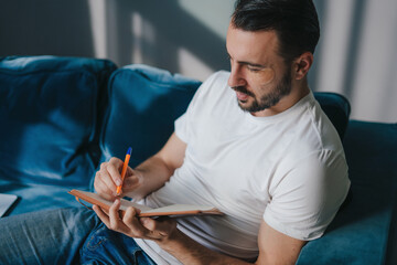 Caucasian man writing down thoughts in journal. Creativeman making notes in a notepad.