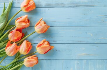   A handful of orange tulips atop a blue wooden table Nearby, a cluster of green leaves - obrazy, fototapety, plakaty