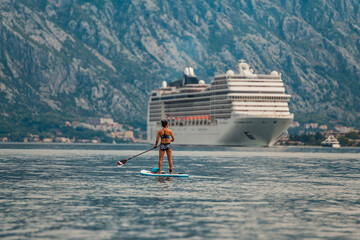 solo paddle boarder in front of a towering cruise ship with a stunning mountainous backdrop