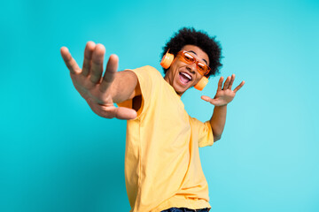 Portrait of overjoyed man with afro hairstyle wear oversize t-shirt in glasses enjoy music in headphones isolated on teal color background - obrazy, fototapety, plakaty