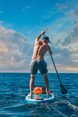 adventurous man paddleboarding in the open sea looking towards the horizon