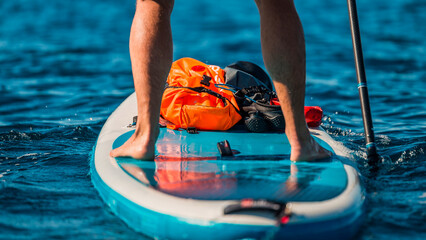 close-up of a man's legs paddleboarding in clear blue waters with safety gear on board
