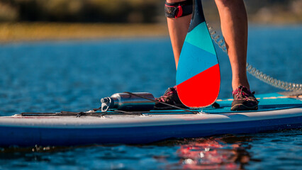 close-up of a man's legs paddleboarding in clear blue waters with safety gear on board