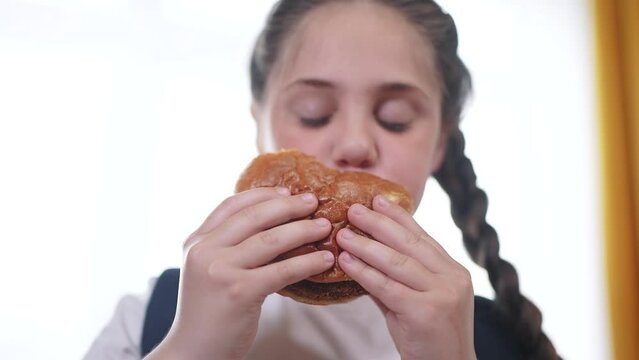 schoolgirl child eating hamburger breakfast at recess. training nutrition lifestyle for schoolchildren fast food concept. schoolgirl child eating breakfast sandwich from a paper bag with a backpack