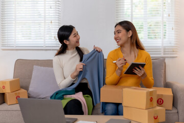 Two smiling women packing clothing items for online shop orders, sharing a joyful moment.