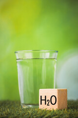 h2o water, Impact of water on the environment, Environmental science concept, Glass of water on green background, wooden block with h2o symbol, Vertical
