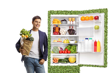 Young man holding a grocery bag and leaning on a green eco-friendly fridge