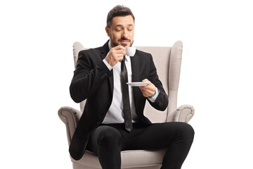Businessman sitting in an armchair and drinking espresso coffee