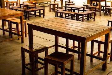 A group of wooden tables and chairs are set up in a room. The tables are empty, and the chairs are...