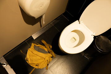 A toilet with a yellow bag on the floor next