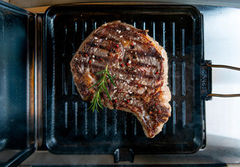 Rib eye beef cooking on cast iron griddle with rosemary and spices