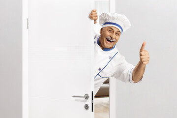Mature chef in a uniform gesturing thumbs up behind a door