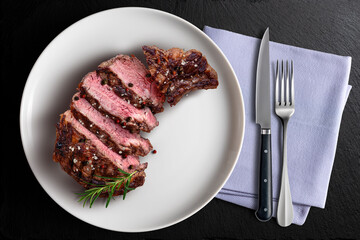 Top view of sliced Rib eye beef in white round plate flavored with knife and fork