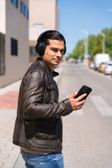 Fototapeta premium Modern and handsome man listening to music with headphones and his cell phone on the street.