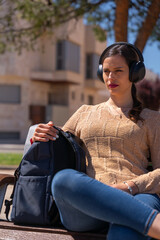 Beautiful woman listening to music with headphones while sitting with her backpack