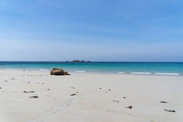 Plage de sable blanc, rochers dispersés, sous un ciel bleu éclatant, avec des eaux d'un turquoise...