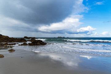 Fototapeta na wymiar Sur le sable mouillé d'une plage bretonne, de beaux reflets des nuages aux couleurs contrastées créent un spectacle enchanteur.