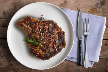 Flavored Whole rib eye beef on white round plate with cutlery and napkin